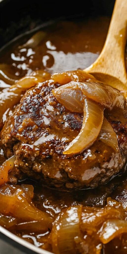 hamburger steaks smothered in a rich onion gravy. The patties are thick, well-browned, and slightly textured, indicating a crispy exterior while retaining a juicy, tender interior.